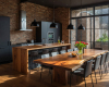 Luxury industrial kitchen featuring a live edge suar wood dining table, a matching waterfall island, minimalist black cabinets, and an exposed brick wall.