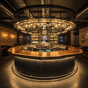 An ultra-luxury industrial bar features a bespoke live edge suar wood top, illuminated with subtle under-lighting.