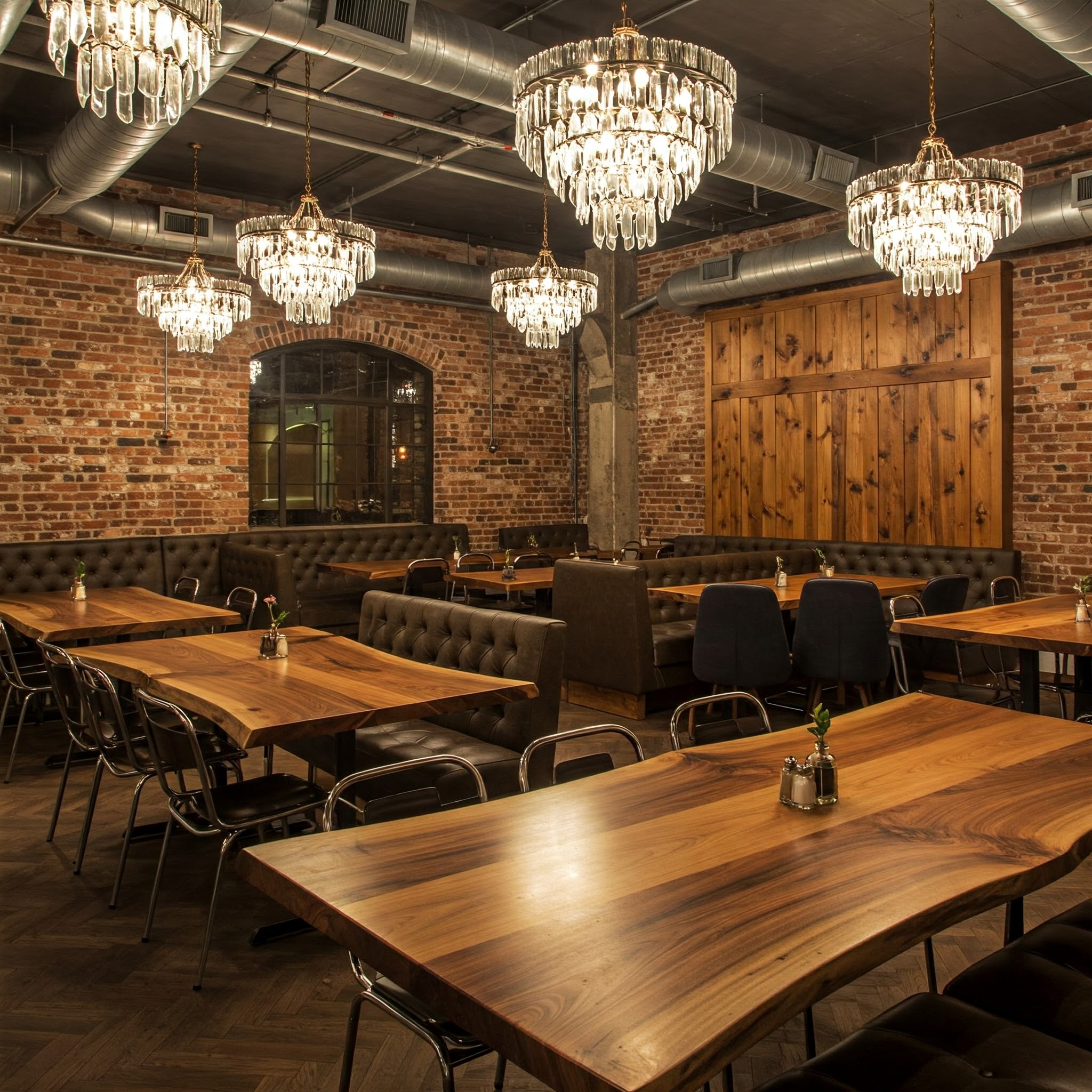 This custom restaurant interior juxtaposes industrial brick walls with the glamour of chandeliers and live edge tables.