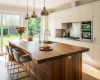 A luxury open-plan kitchen's focus is a live edge waterfall island with a breakfast bar and minimalist white cabinets.